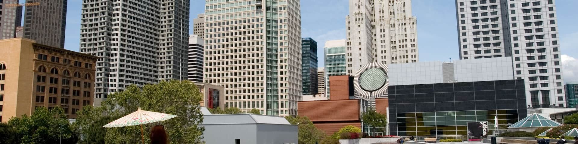 A cityscape with tall buildings, a fountain, and a tiled plaza.
