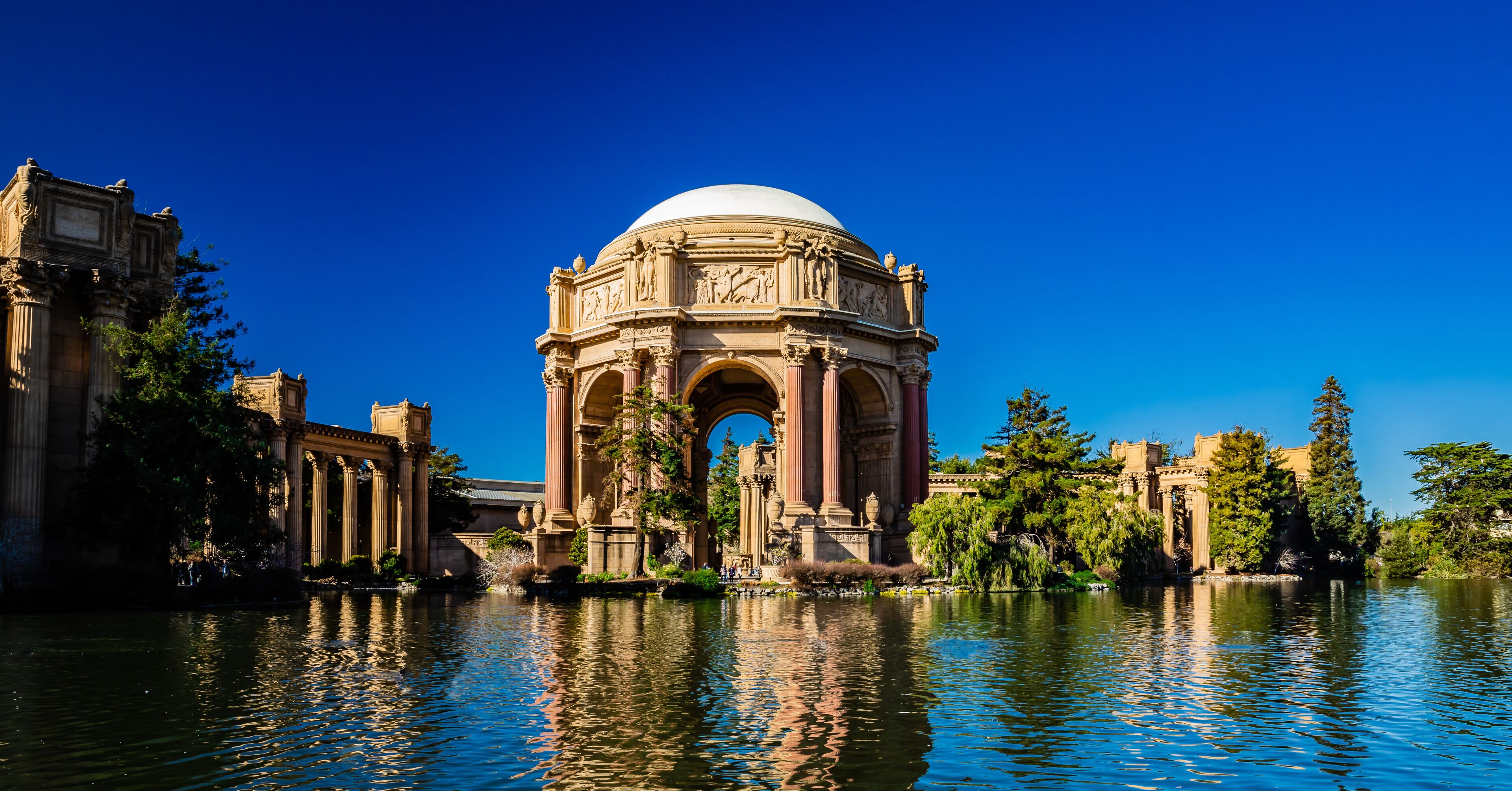 A historic building with a dome and arches, surrounded by a body of water and trees.