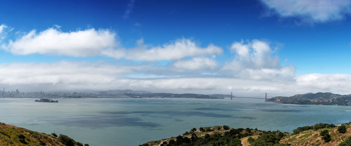 A coastal cityscape with a prominent bridge in the distance.