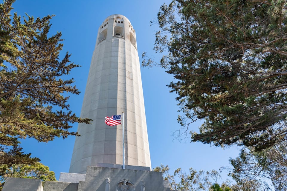 A tall, cylindrical monument with an American flag, surrounded by trees.