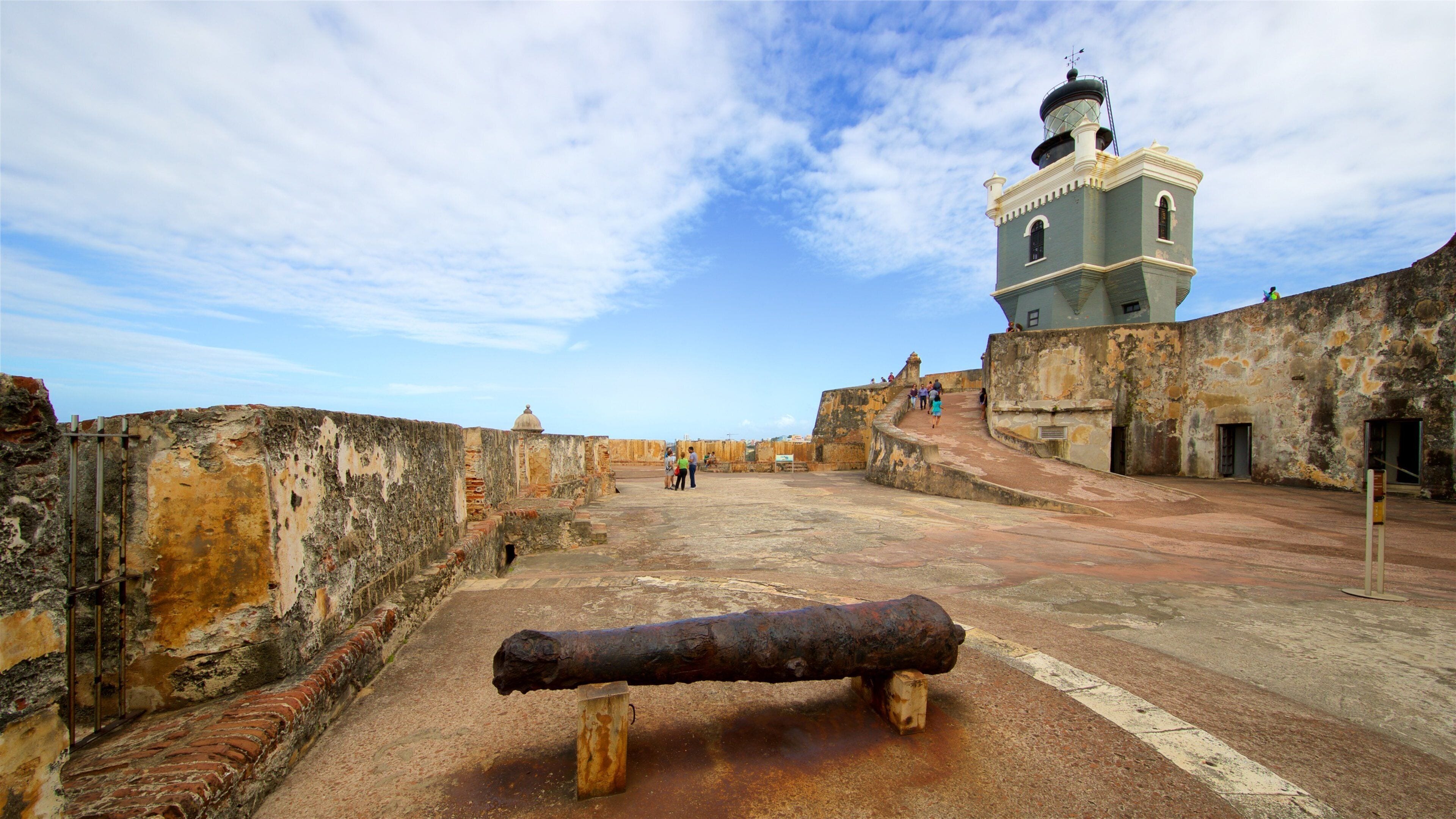 A historic fort with a weathered cannon, a watchtower, and visitors exploring the site.