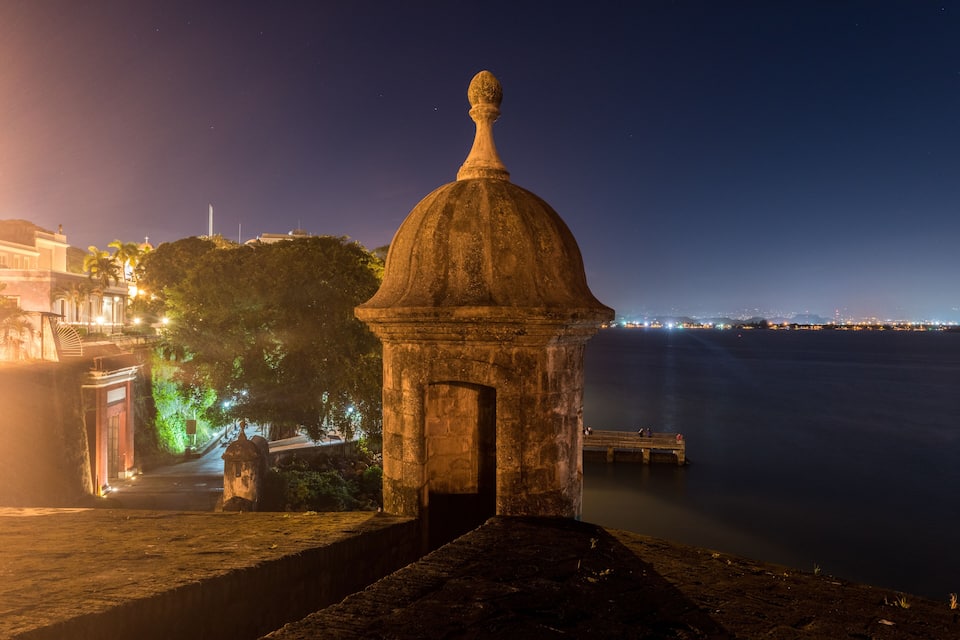 A stone structure with a dome and a statue on a waterfront at night.
