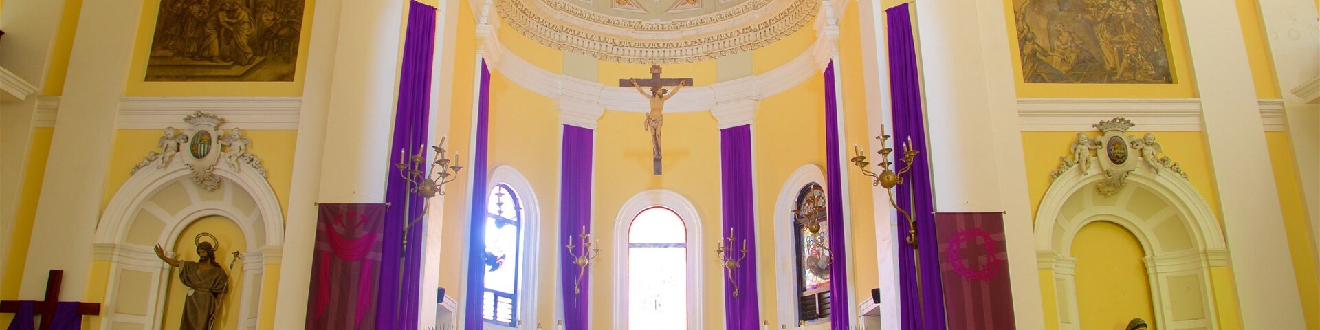 Interior de igreja com cruz, altar e estátuas.