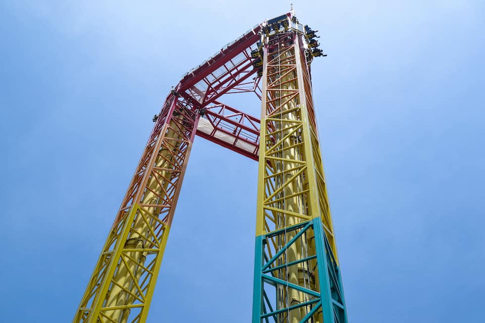 A tall amusement park ride with a red and yellow structure against a clear blue sky.