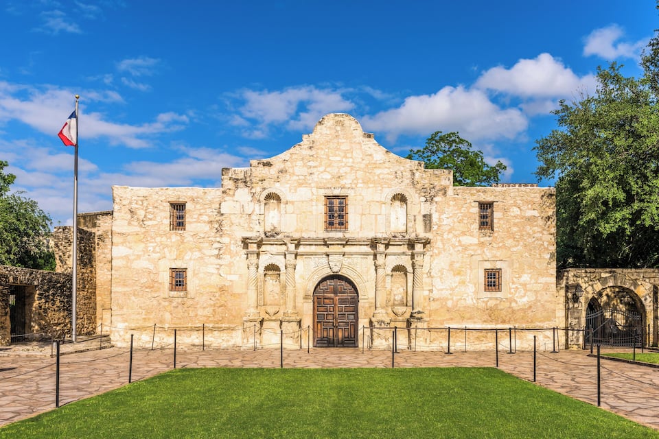 A historic stone building with a prominent arched entrance and a flagpole with a flag.
