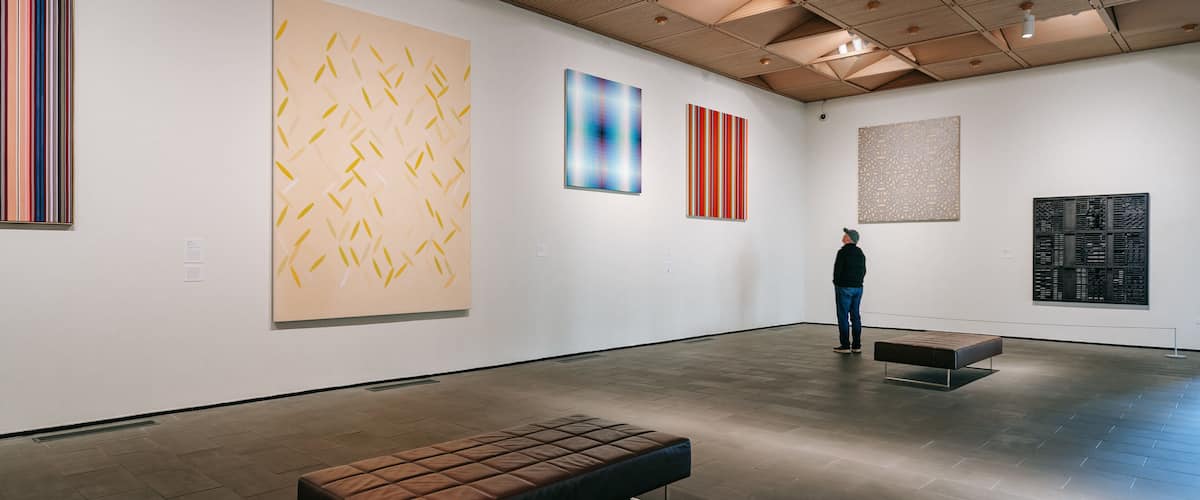 An art gallery with abstract paintings on the walls and a bench in the center.