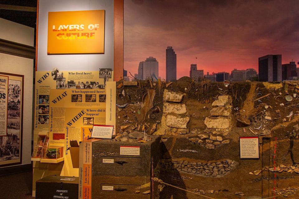 An archaeological dig site with informational posters and a cityscape backdrop.