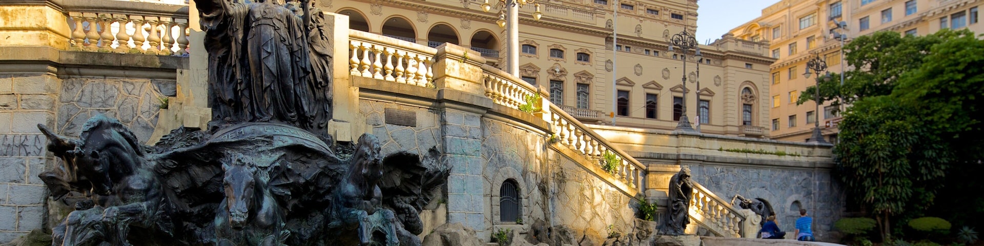 Estátua equestre em bronze com uma fonte na frente, diante de um edifício histórico com arquitetura clássica.