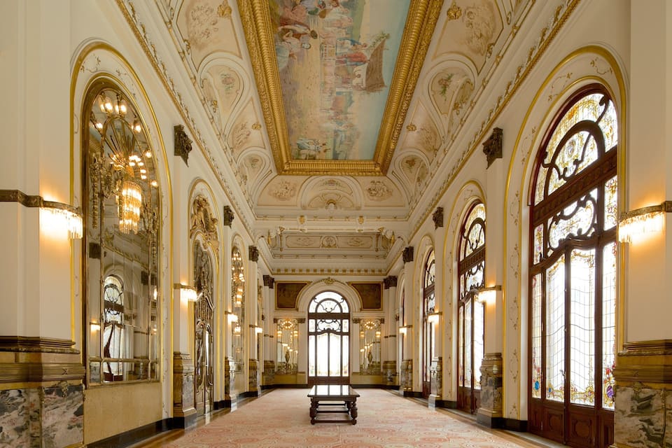 A grand hallway with ornate ceilings, large windows, and a marble floor.