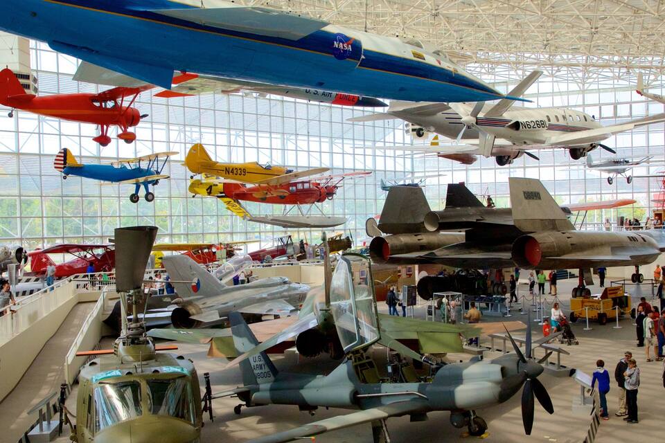A museum with various aircraft on display, including fighter jets and biplanes.