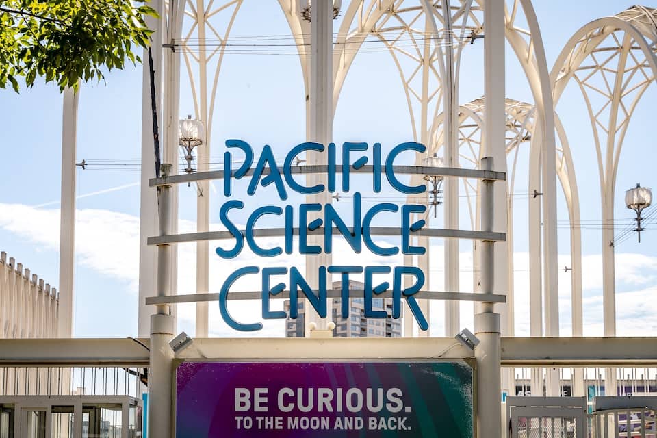 A sign for the Pacific Science Center with the tagline "Be curious. To the moon and back."