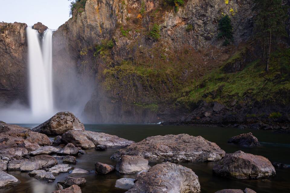 Una cascata che si getta da una scogliera rocciosa in un fiume circondato da massi.