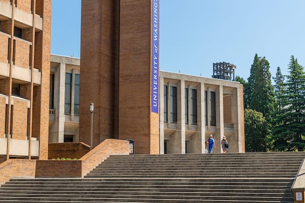 Un bâtiment universitaire orné d’une grande banderole indiquant « Université de Washington », caractérisé par son architecture en briques et un escalier menant à l’entrée.