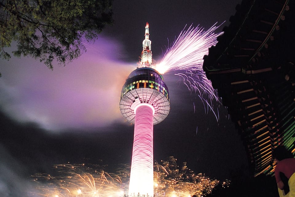 Een toren met een bolvormig uitkijkplatform, omringd door vuurwerk.