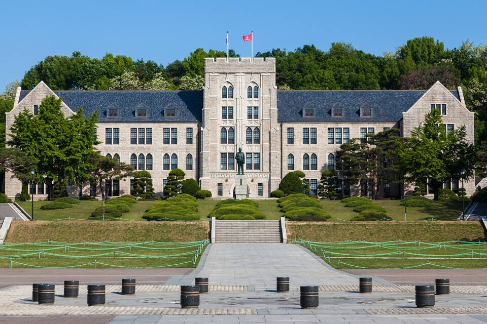 A large stone building with a central tower, surrounded by well-maintained lawns and trees.