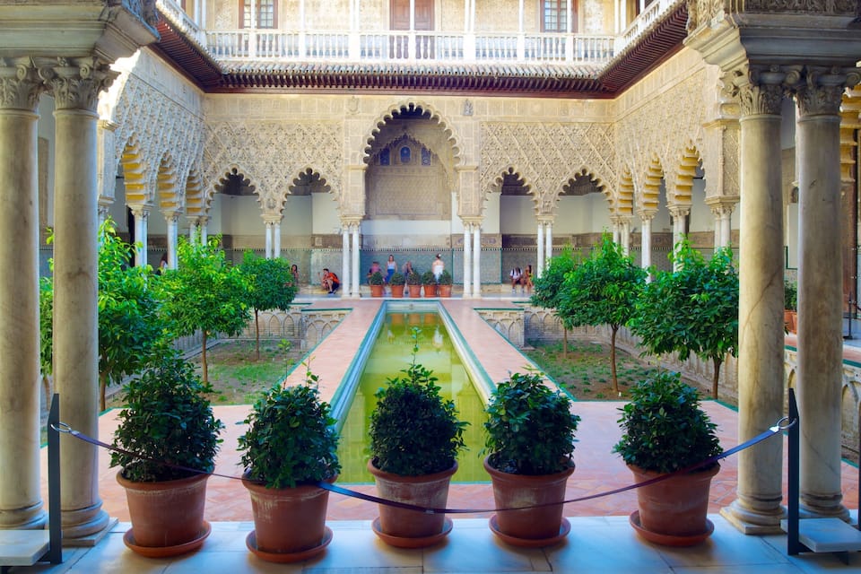 A courtyard with a central water feature, surrounded by columns and potted trees.