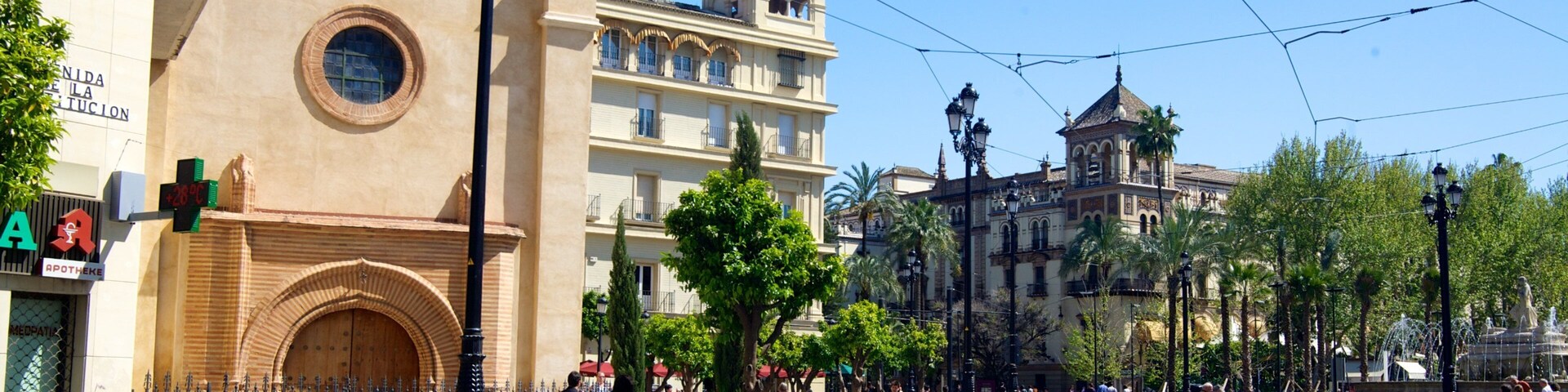 Uma praça urbana ensolarada, com linhas de bonde, edifícios históricos e pedestres.