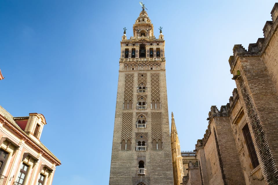 A tall, ornate tower with intricate patterns and a statue on top, surrounded by historic buildings.