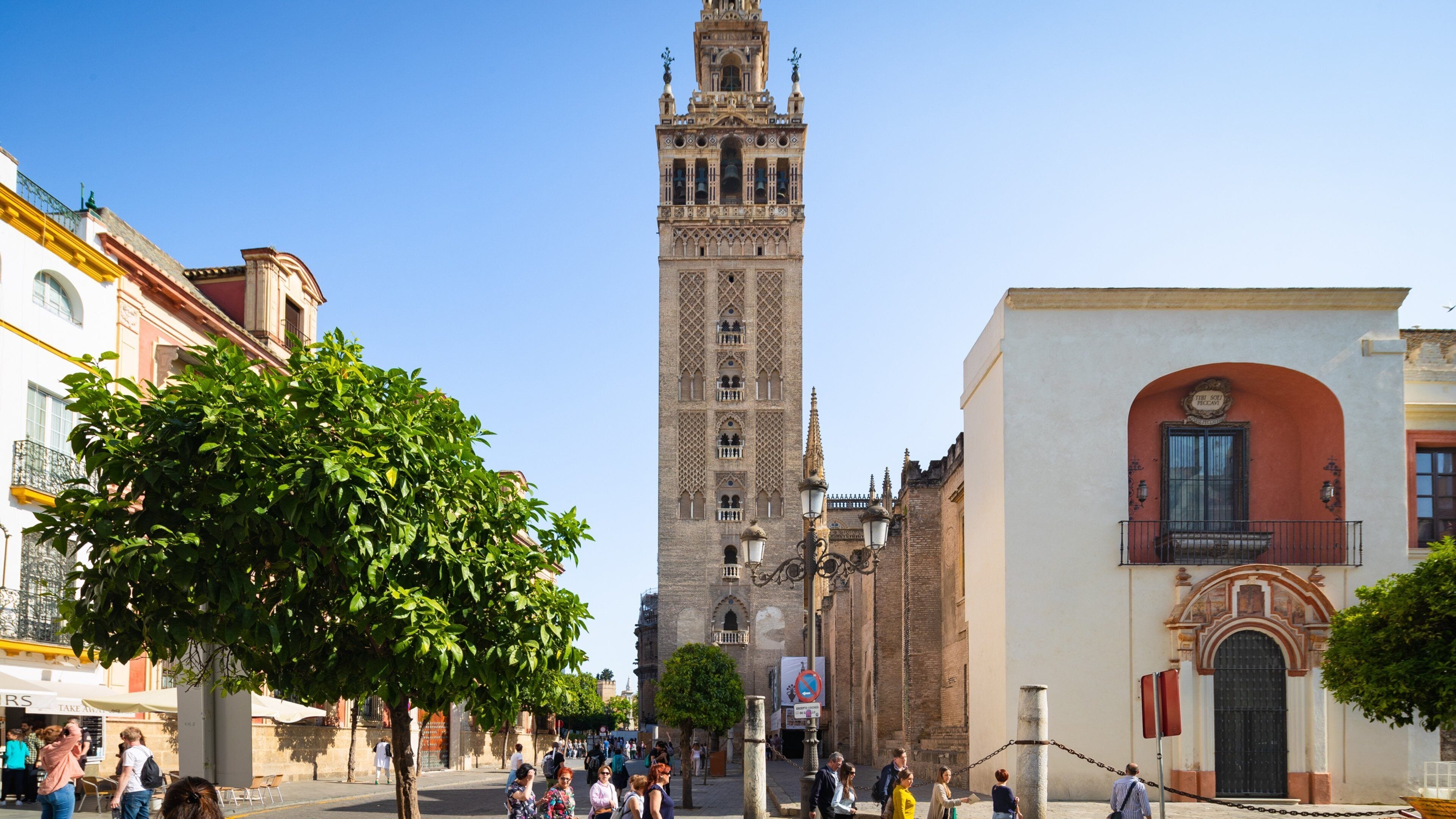 Una torre storica con architettura elaborata, una vivace strada con pedoni e un insieme di edifici tradizionali e moderni.