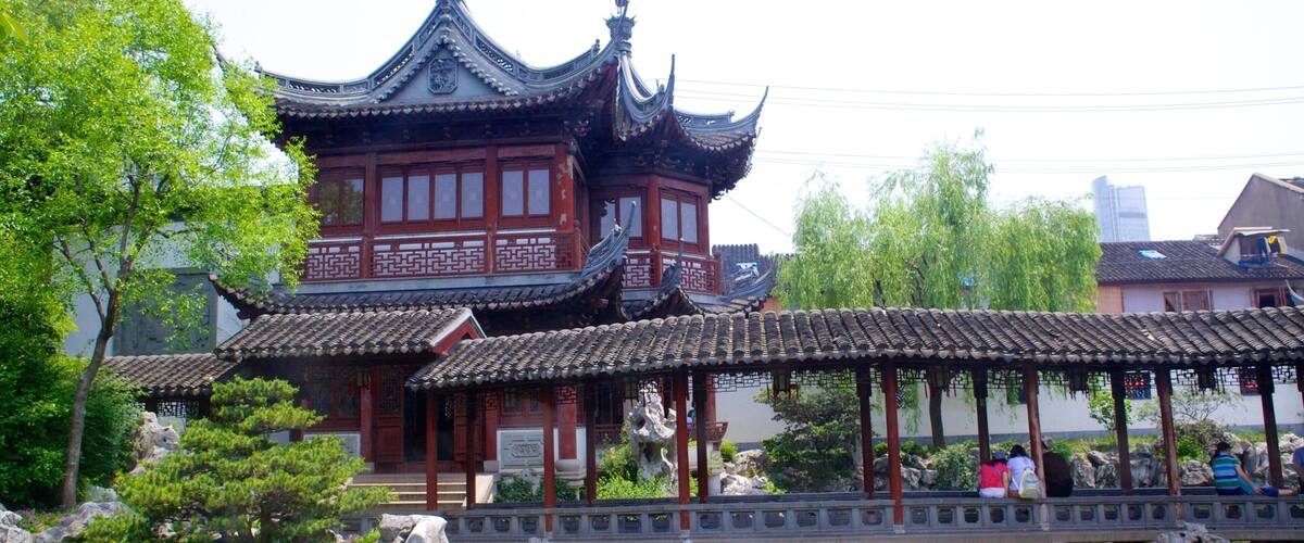 A traditional Chinese building with ornate architecture, a stone bridge, and a pond with rocks.