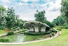 Una struttura architettonica moderna circondata da uno stagno con ninfee, palme e un giardino curato.