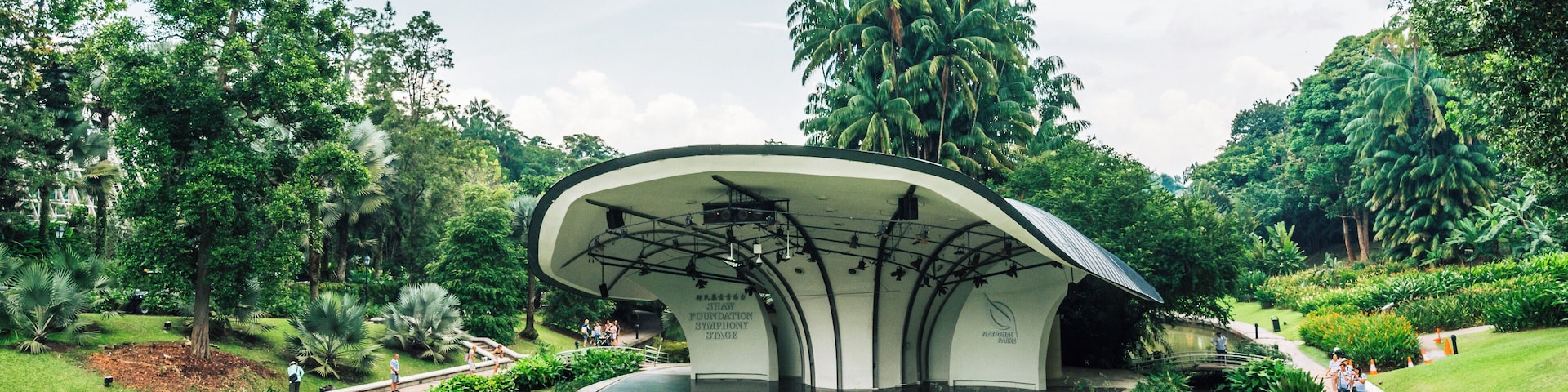 A modern architectural structure surrounded by a pond with lily pads, palm trees, and a well-maintained garden.