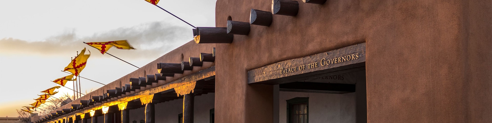 Flags flying above the Palace of the Governors, Santa Fe Plaza, State Capital of New Mexico at sunset on a spring evening. Adobe structure and historical Spanish seat of government in the Southwest.