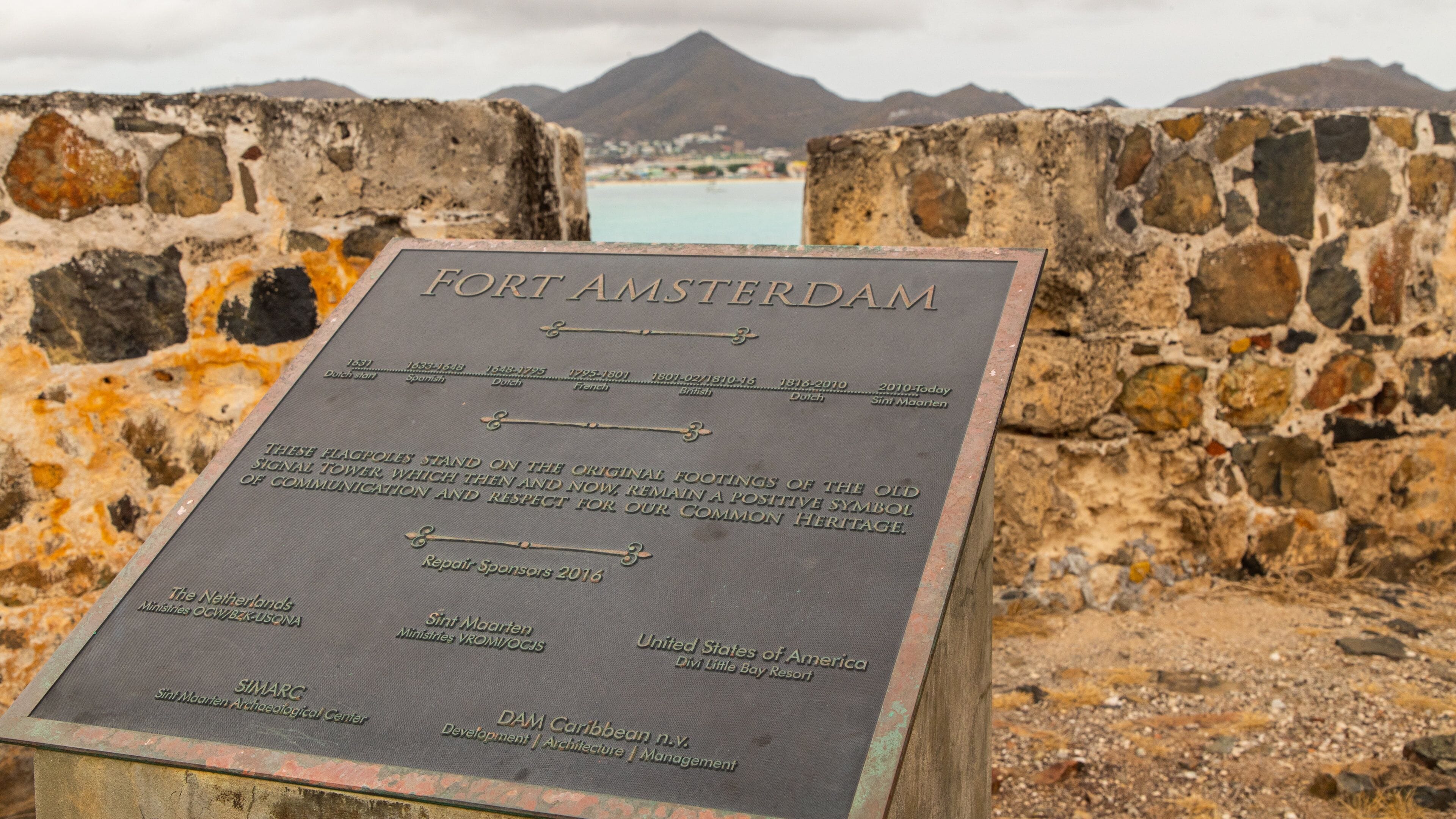 A historical plaque at Fort Amsterdam with a view of the surrounding landscape and mountains.