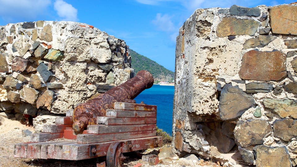 A rusted cannon in a stone fortification with a clear view of the sea and a hill in the background.
