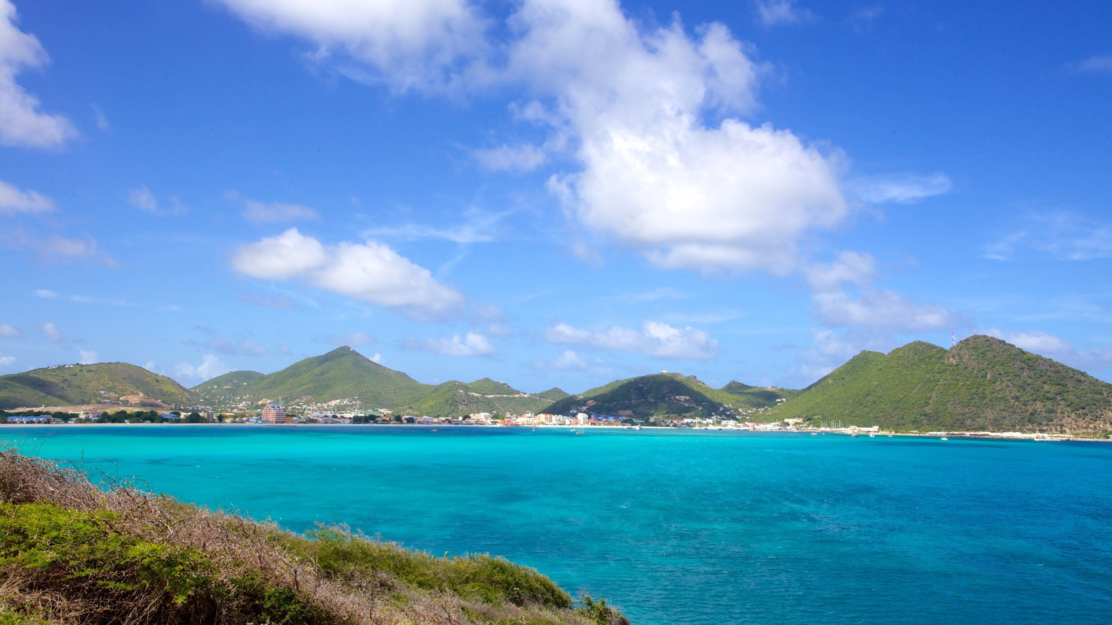 A coastal landscape with turquoise waters, green hills, and a clear blue sky.