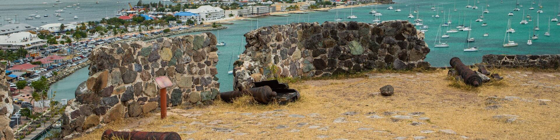A coastal town with a historic fort, a marina with boats, and a distant mountain.