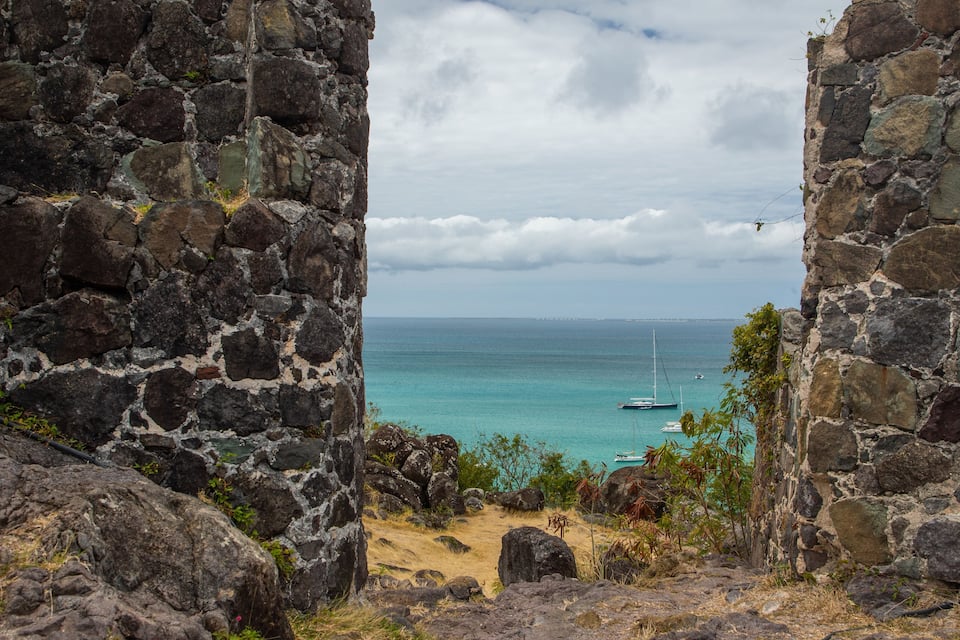 A stone archway leading to a turquoise sea with boats.