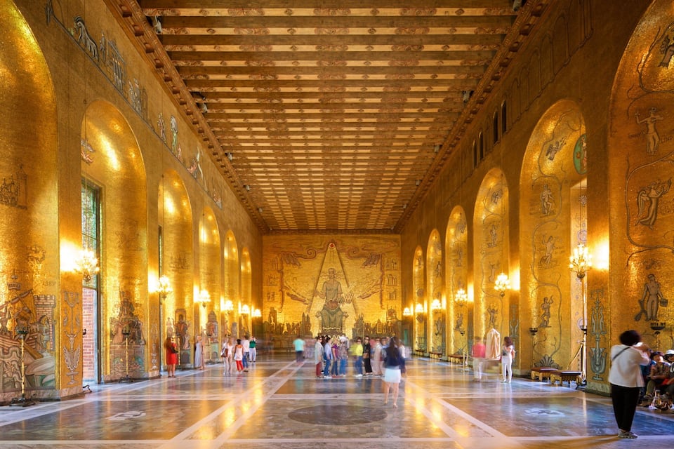 Un salón imponente con paredes y techo dorados, con frescos intrincados y arcos.