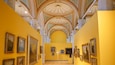 A gallery with yellow walls and a high ceiling with intricate designs.