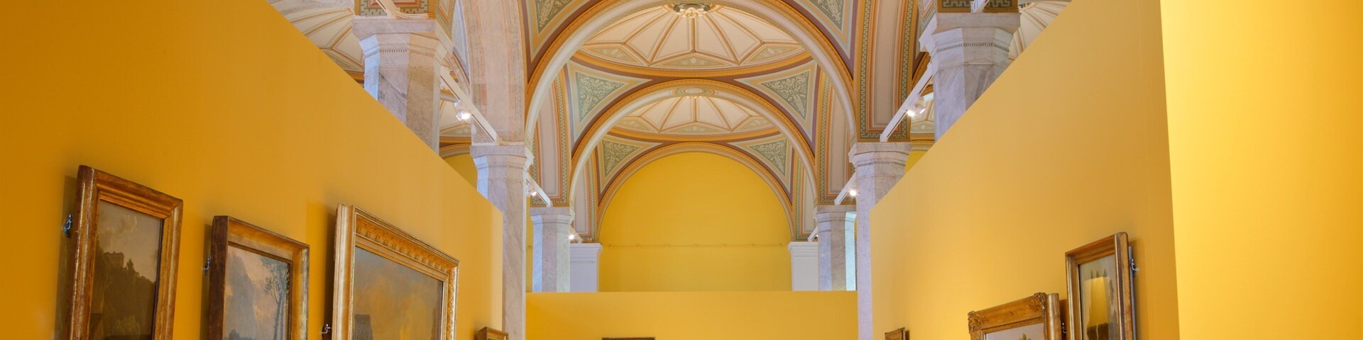 A gallery with yellow walls and a high ceiling with intricate designs.