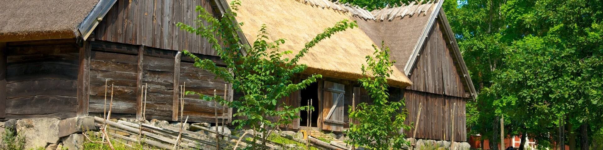 Two wooden buildings with thatched roofs surrounded by greenery.