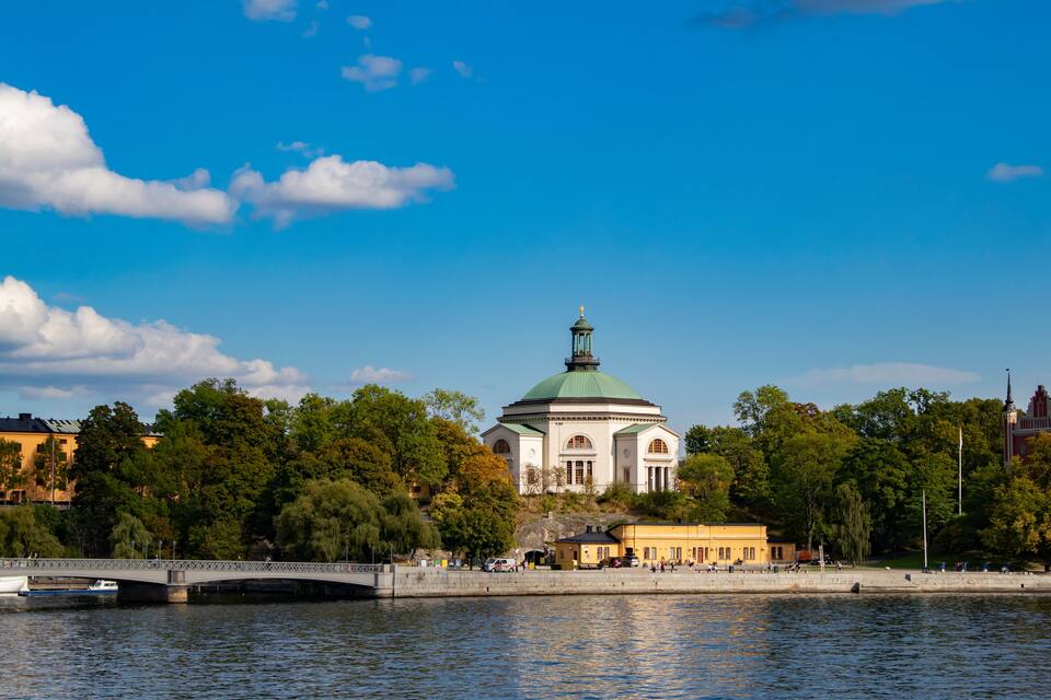 A river with a bridge, a domed building, and trees.