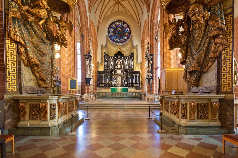 An ornate church interior with a checkered floor, golden statues, and a central altar.