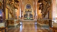 An ornate church interior with a checkered floor, golden statues, and a central altar.