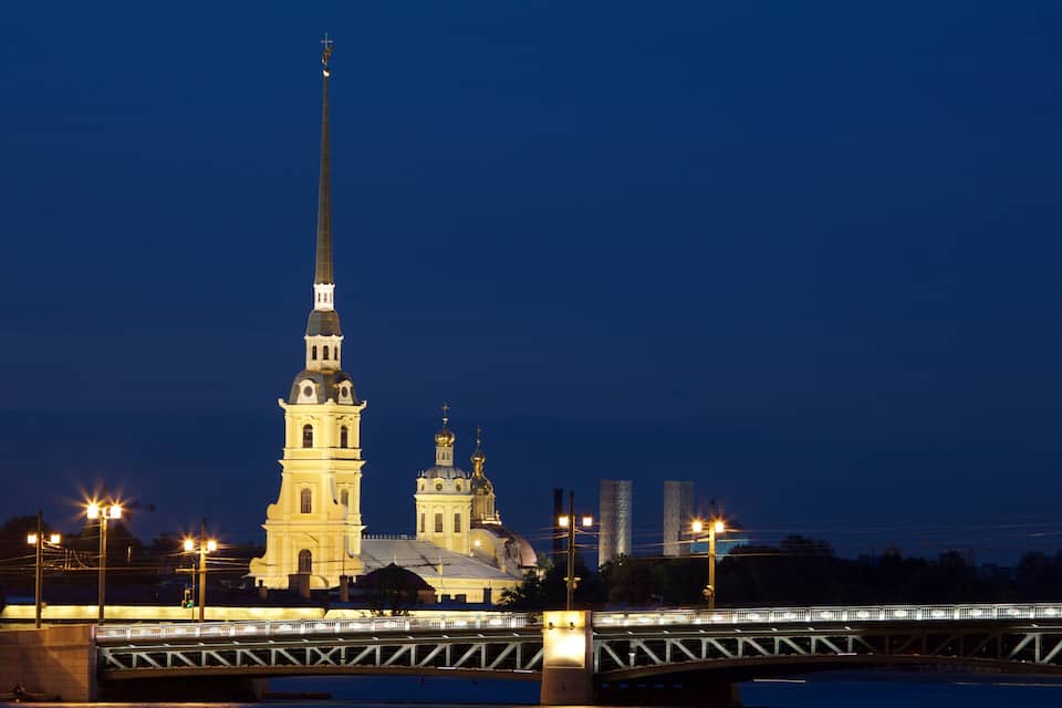 A lit church with a tall spire and a bridge in the foreground.