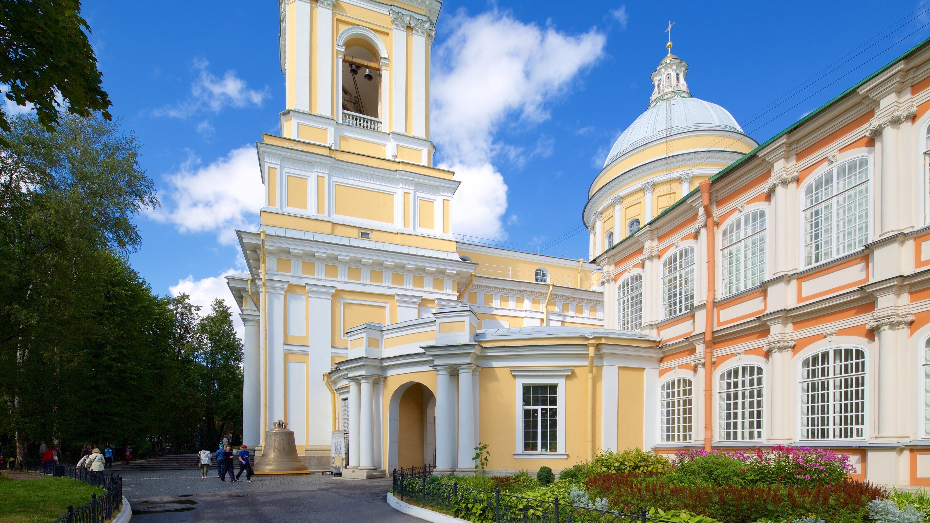 A historic yellow building with a bell tower and a dome, surrounded by greenery and a clear blue sky.