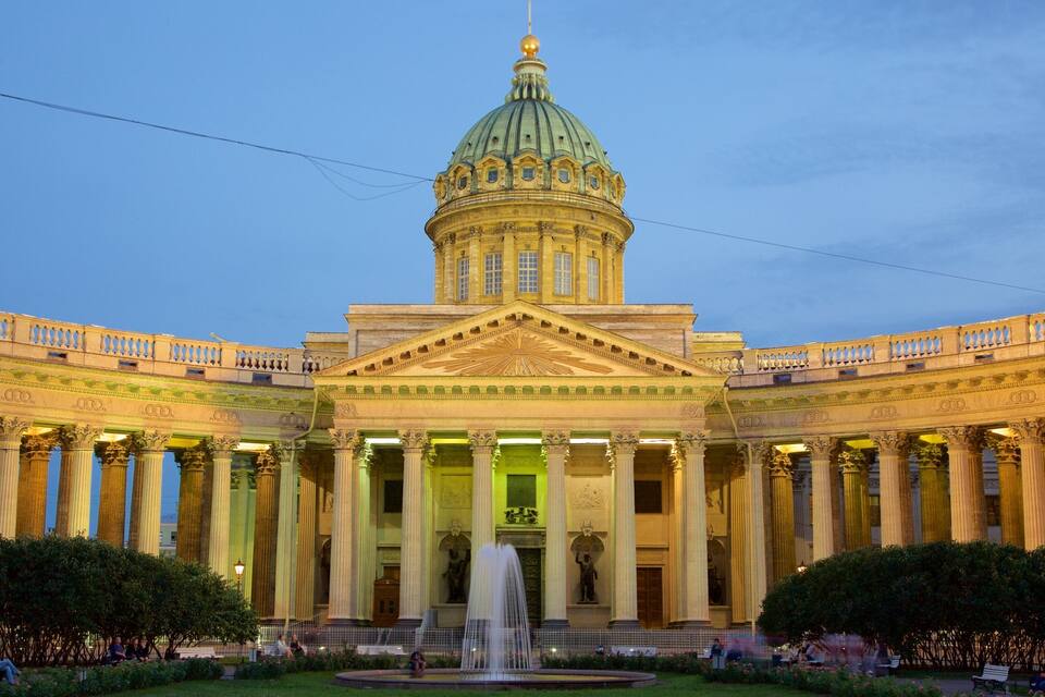 A grand neoclassical building with a large dome and columns, a fountain in the center, and a well-maintained garden.