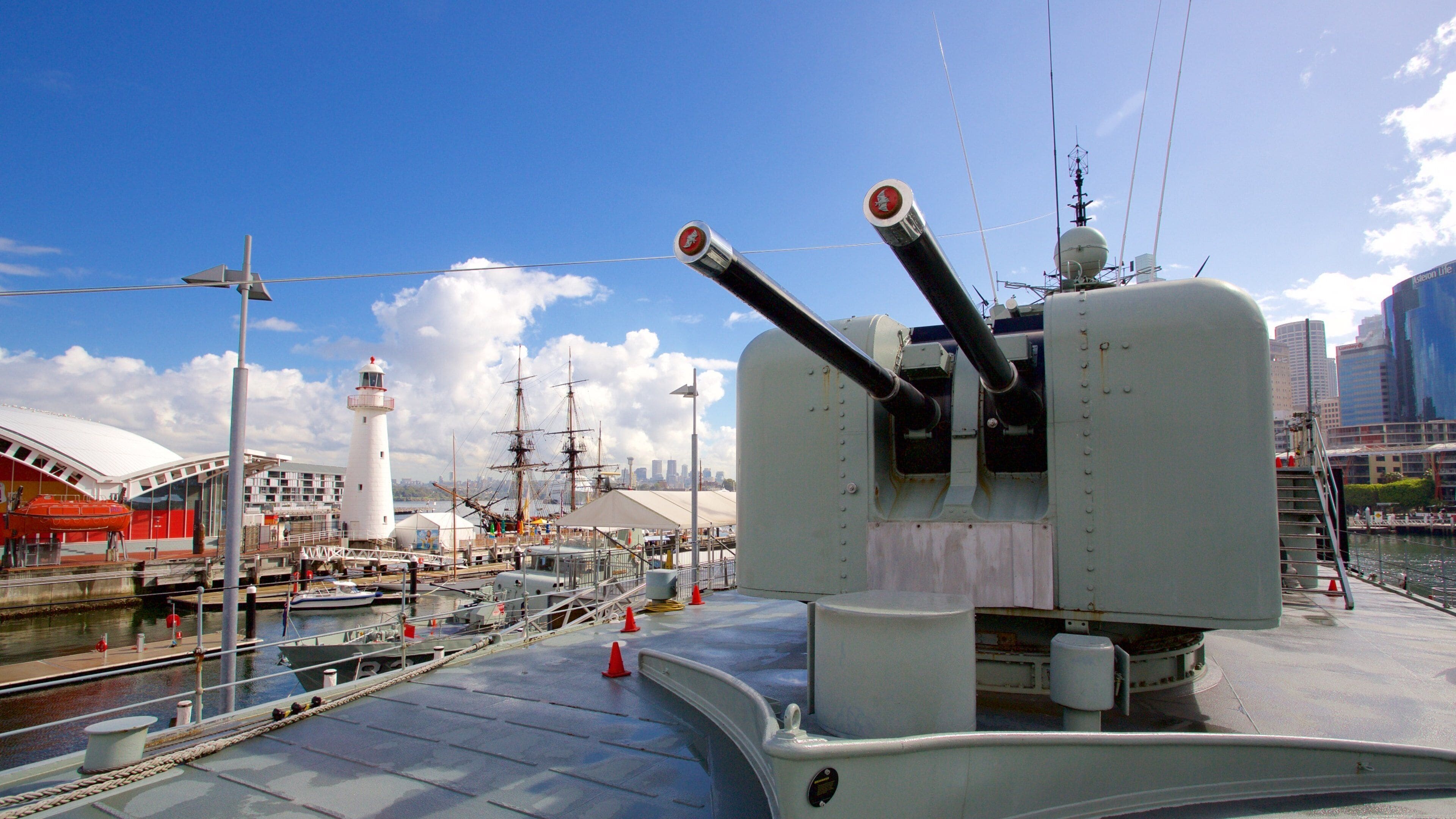 A ship's deck with a large gun turret, a lighthouse, and a city skyline in the background.