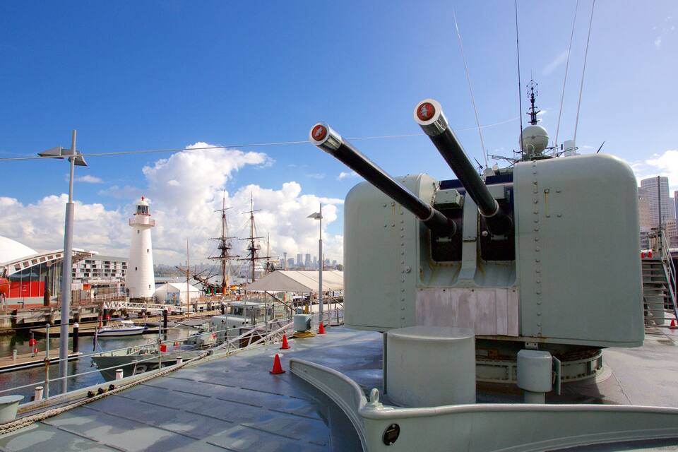 A ship's deck with a large gun turret, a lighthouse, and a city skyline in the background.