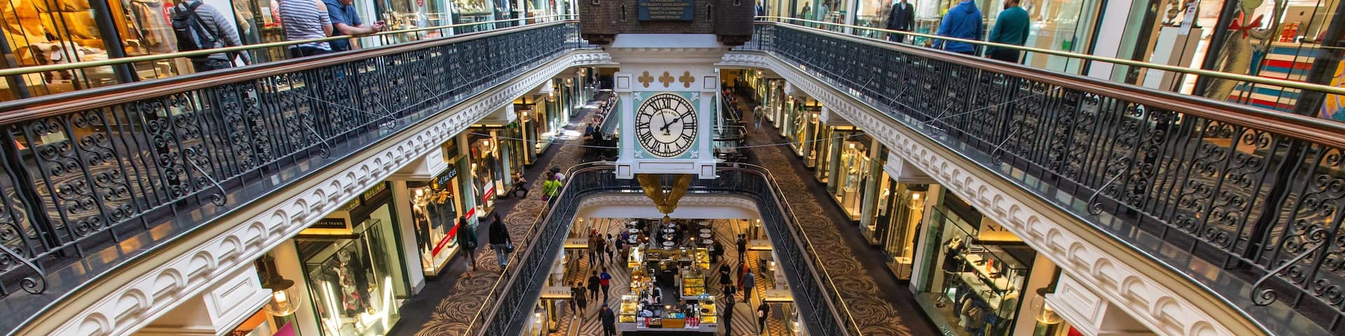 A multi-level shopping mall with ornate railings, a large clock, and various stores.