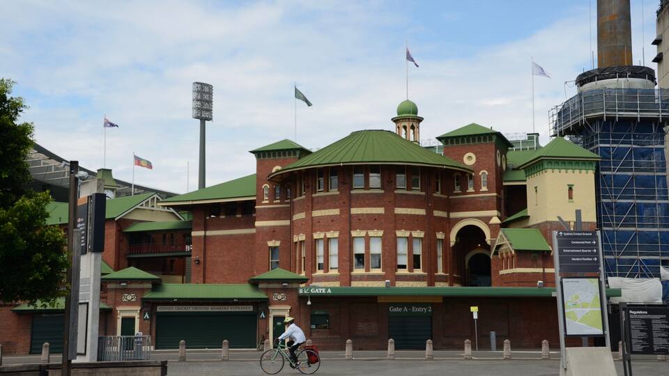A historic brick building with green roofs, a cyclist, and flags.
