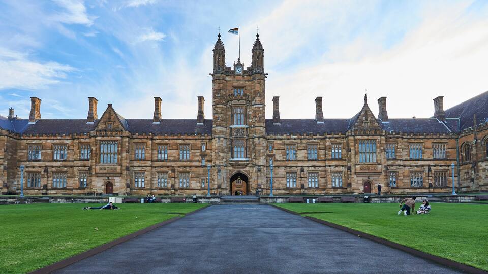A large historic building with a central tower, symmetrical windows, and a paved walkway leading to the entrance.