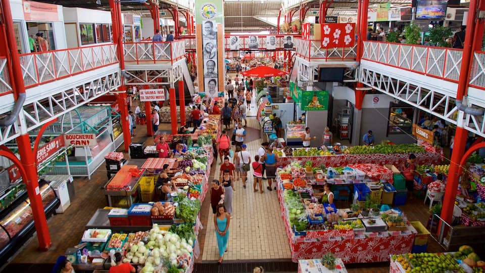 An indoor market with red and white railings, various stalls selling fruits and vegetables, and people shopping.