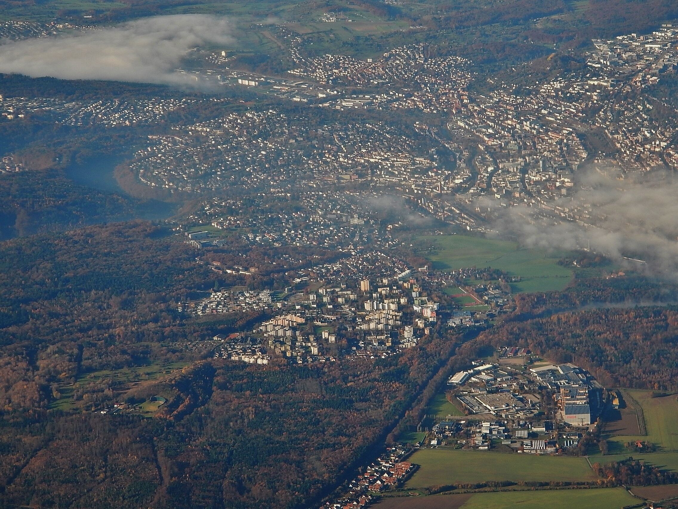 An aerial view of a densely populated town with a river running through it, surrounded by forested hills.