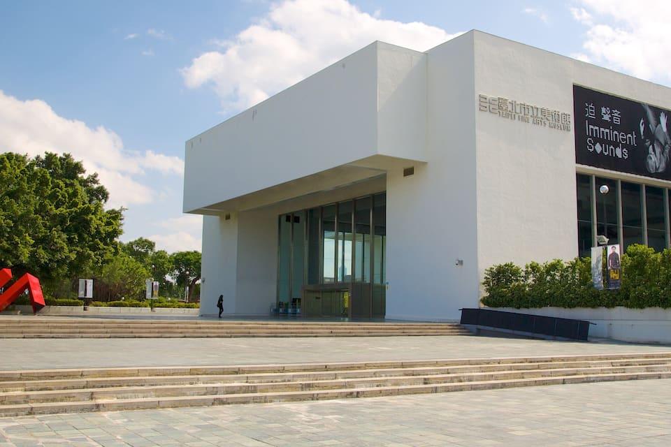 Un bâtiment moderne doté d’une grande entrée en verre, entouré d’escaliers et de verdure.